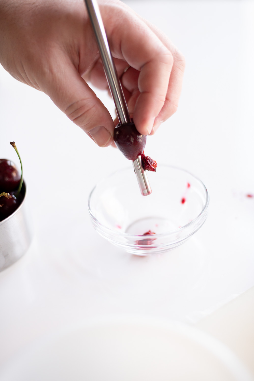 a man pits a cherry using a metal straw in preparation for making semi homemade cherry hand pies