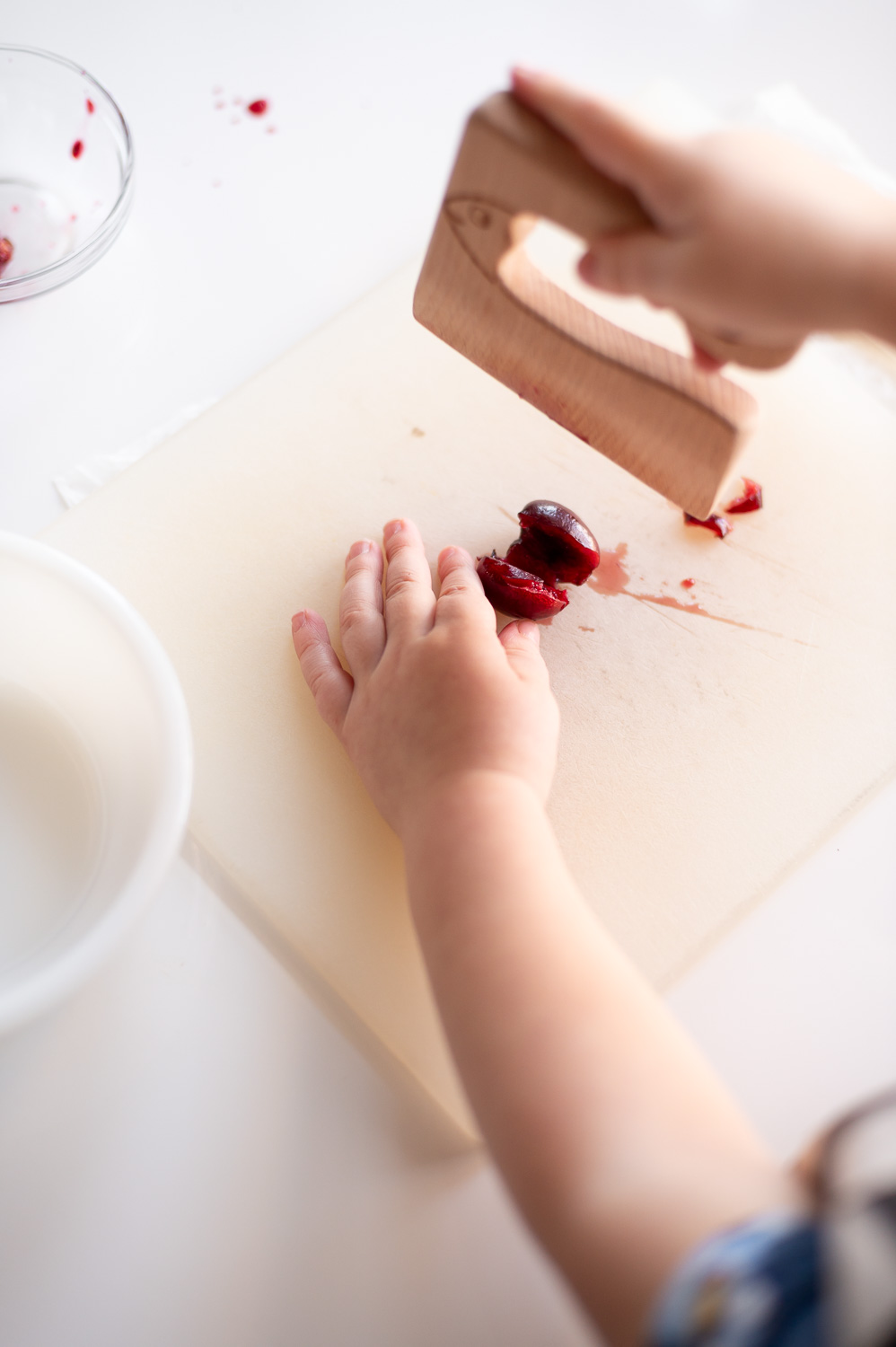 a toddler chops up cherries with a wooden practice knife to help make easy cherry hand pies