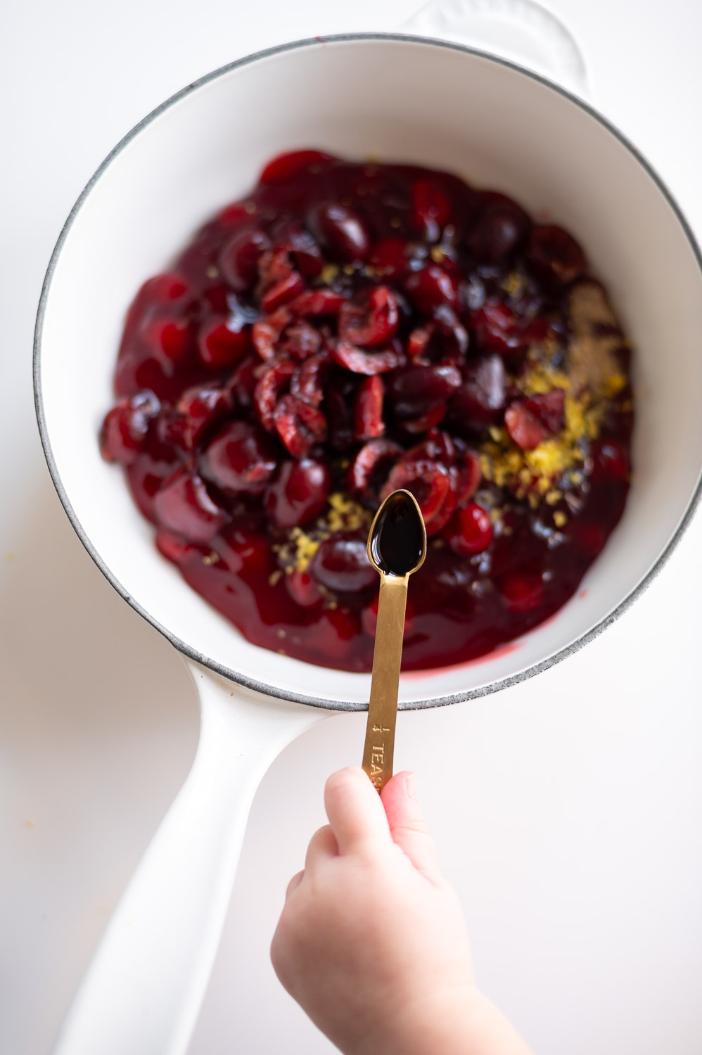 a toddler adds vanilla extract to a saucepan to upgrade canned cherry pie filling for cherry hand pies