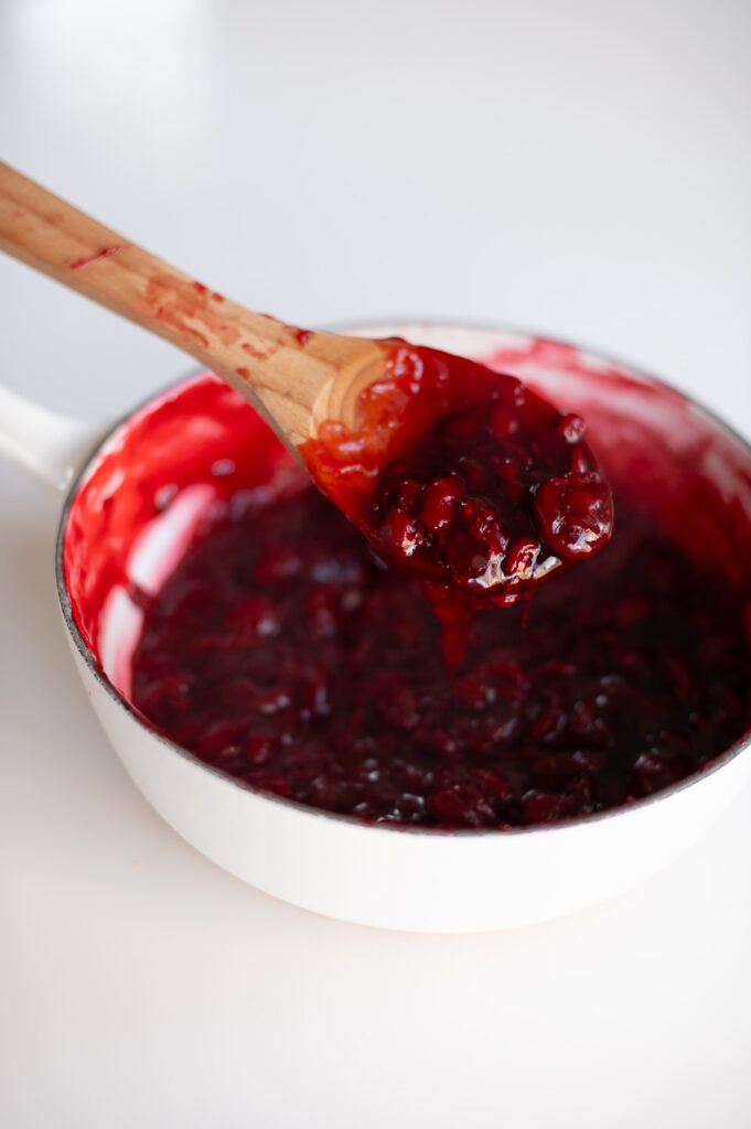 a spoon shows the consistency of upgraded canned cherry pie filling straight off a simmer on the stovetop having reduced down.