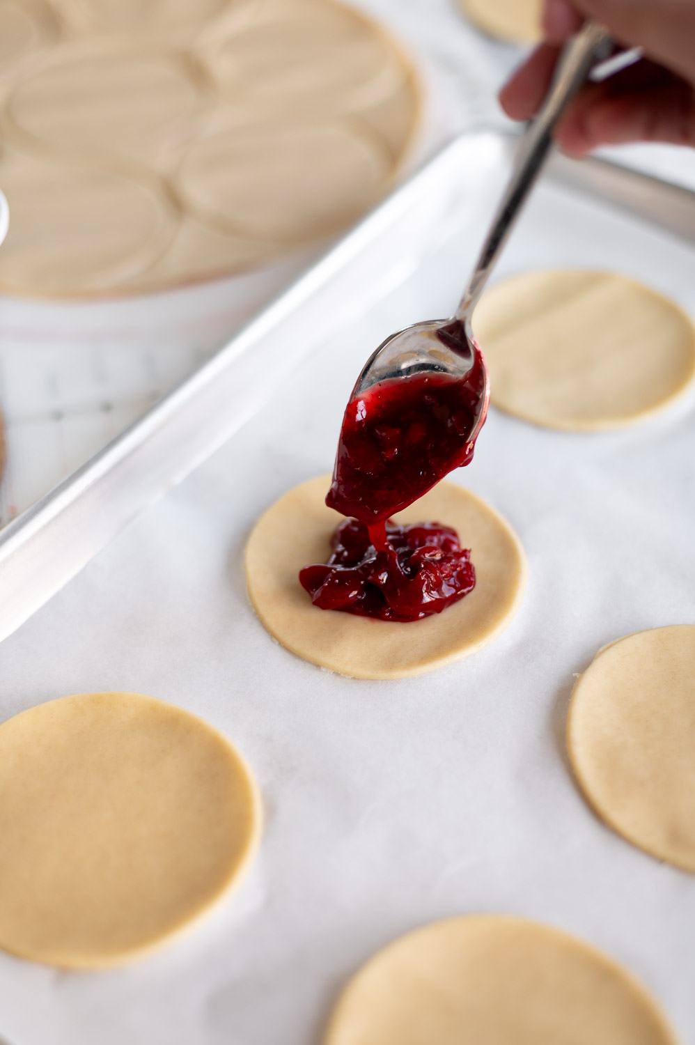 a spoonful of upgraded canned cherry pie filling is added to the center of store bought premade pie dough in order to make easy cherry hand pies