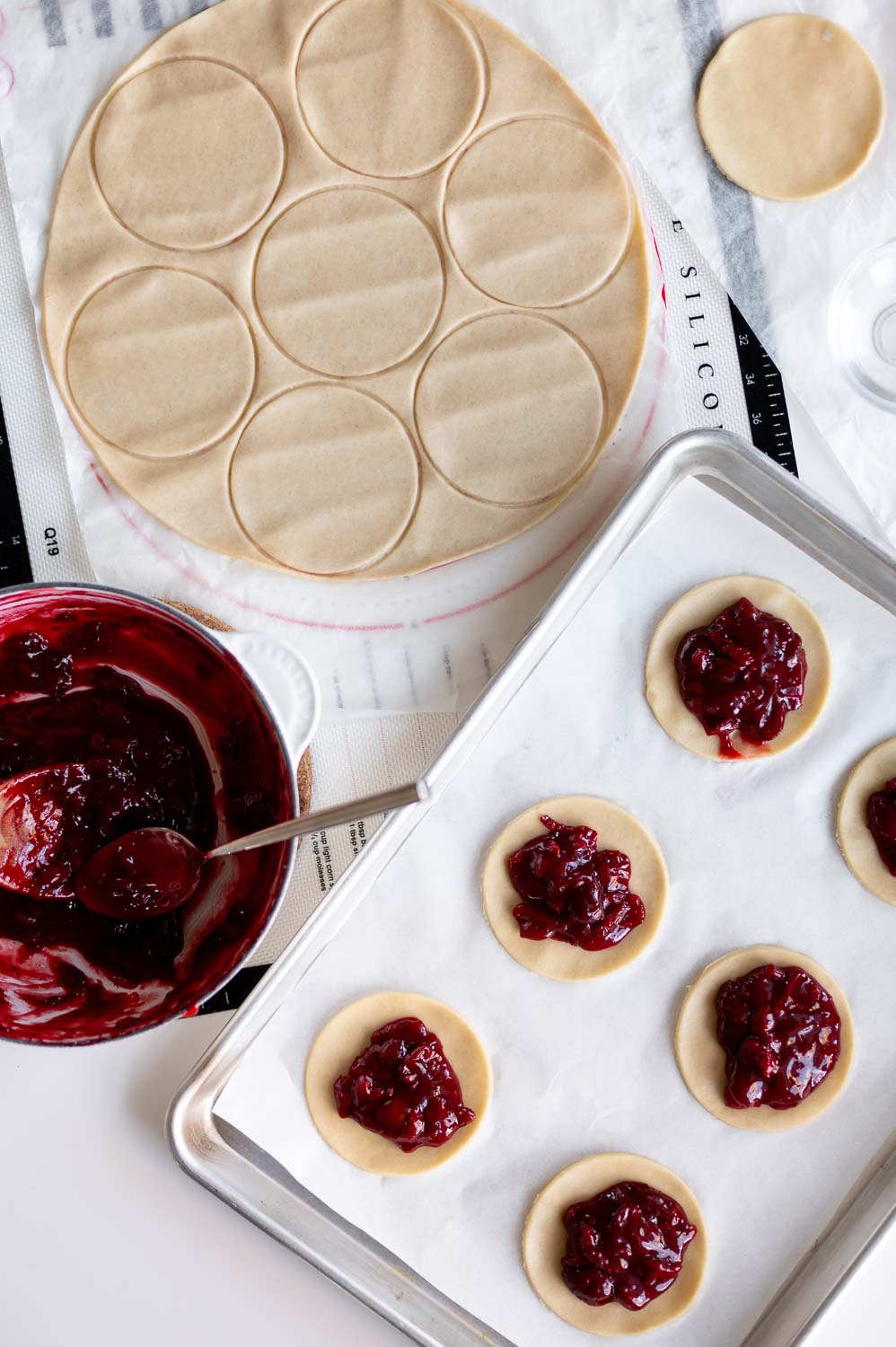 a baking sheet is filled with 3" round premade pie dough cut outs topped with a spoonful of upgraded canned cherry pie filling for making cherry hand pies