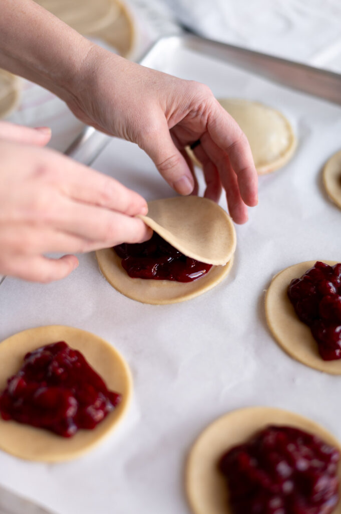 a woman places pie dough on top a cherry hand pie to seal the upgraded canned cherry pie filling inside before baking