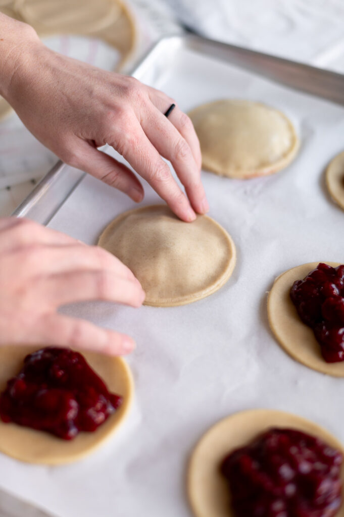 A woman presses down on the edges of the lid of a cherry hand pie to help seal the top and bottom of the pie together