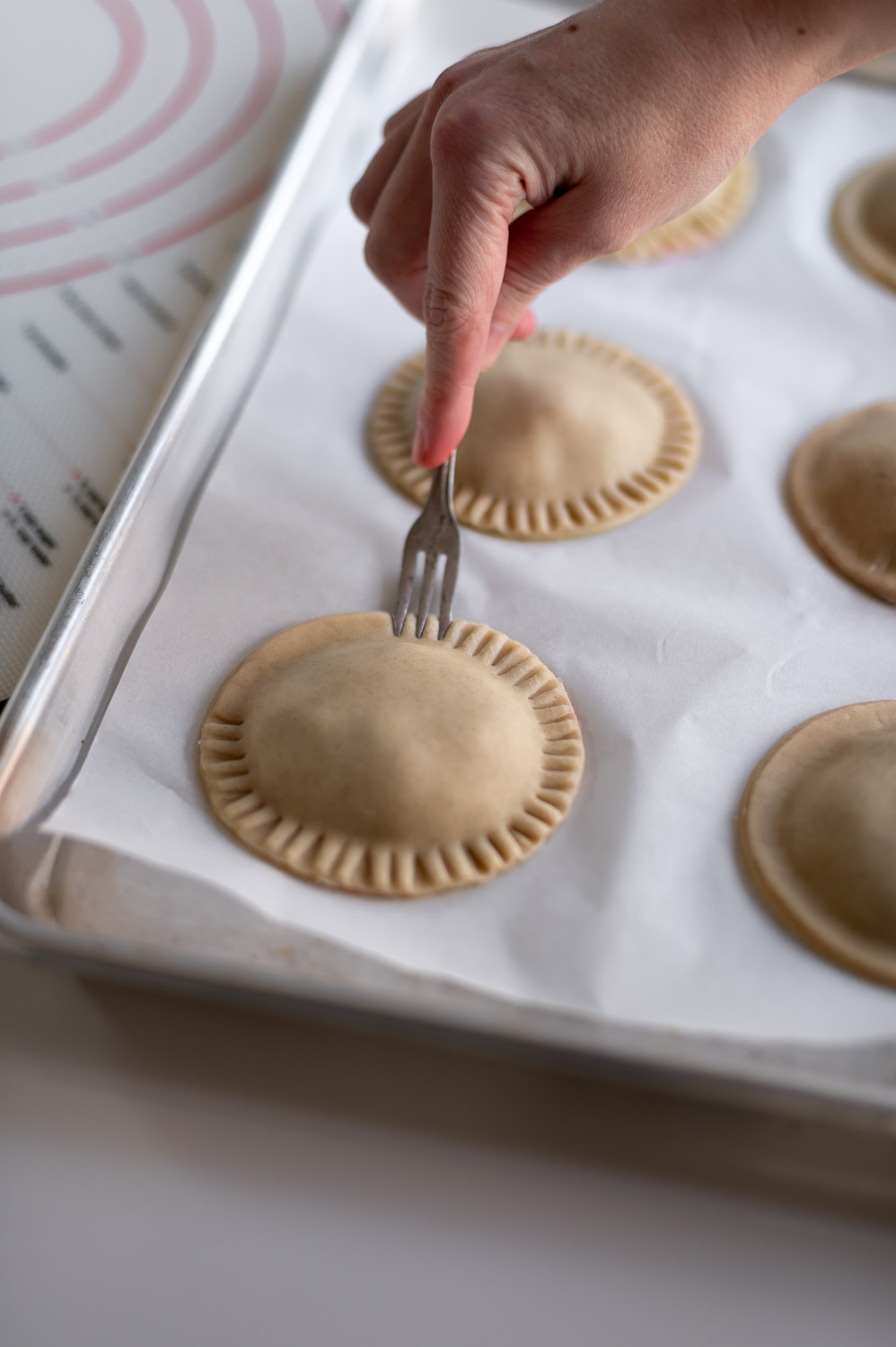 A woman seals the edges of easy cherry hand pies together by crimping them with a fork
