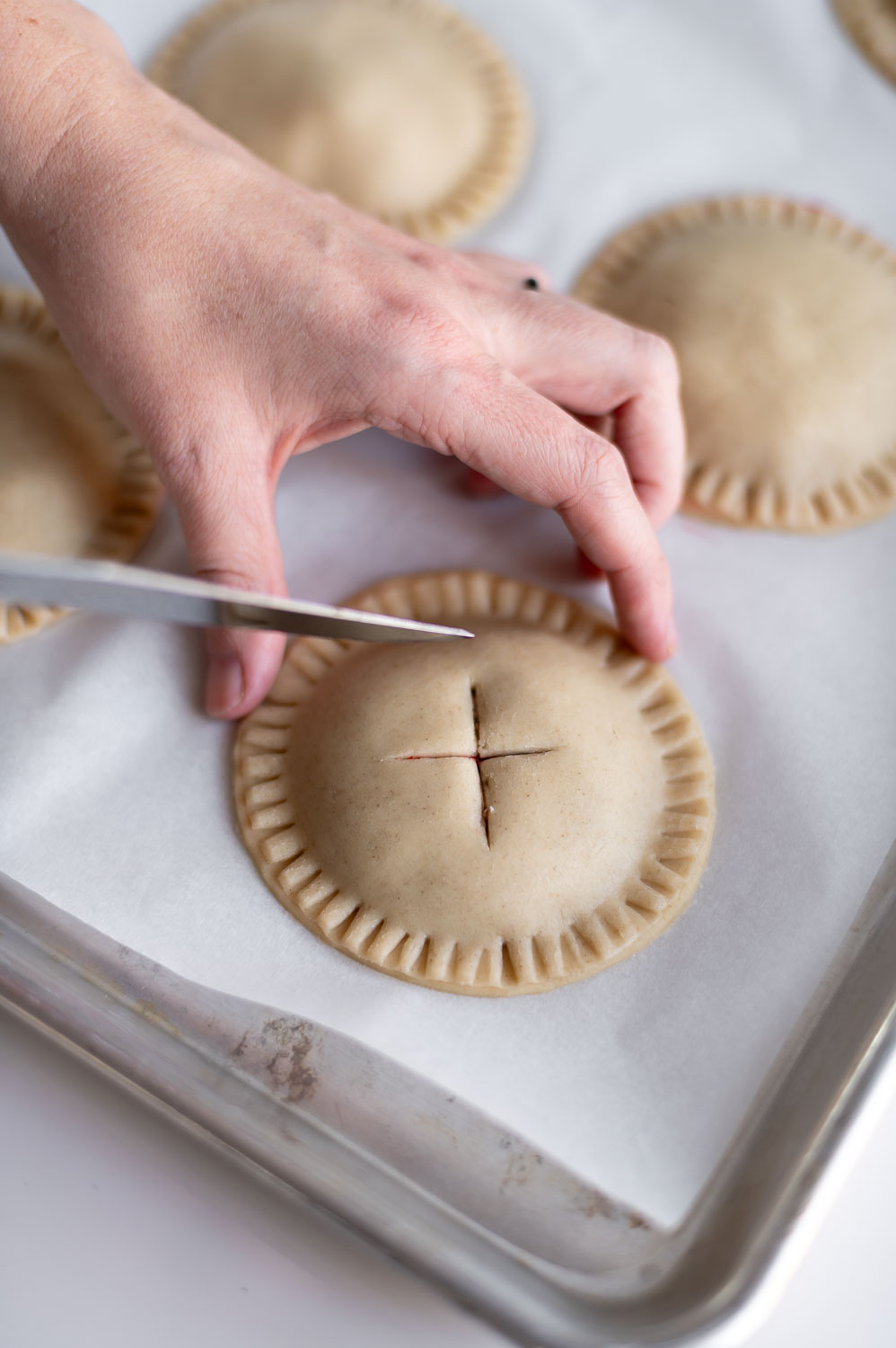 a woman places the lid of a pie onto a easy  cherry hand pie before baking them