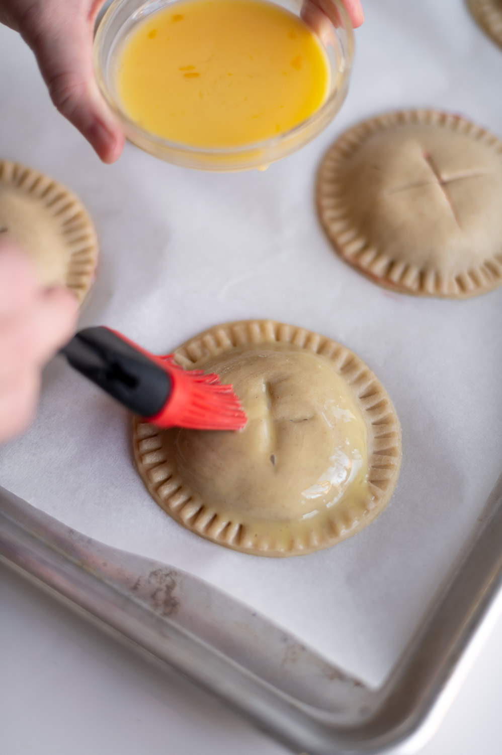 a woman tops cherry hand pies with an egg and milk egg wash prior to baking