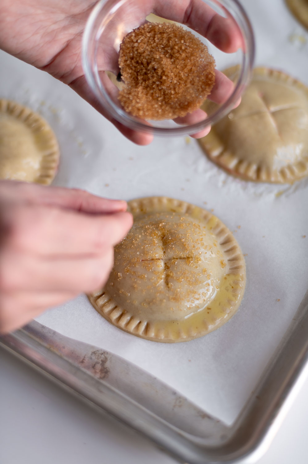 a woman tops easy cherry hand pies with turbinado sugar prior to placing them in the oven to bake