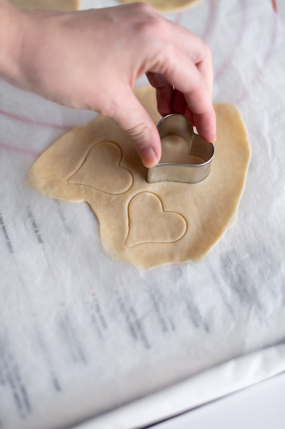a woman cuts small heart shapes out of premade store bought pie to do decorate Valentine's day cherry hand pies
