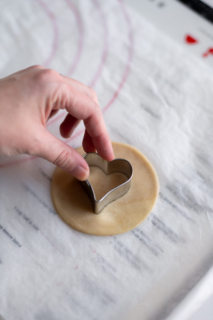 a woman cuts a heart shape out of the center of a Valentine's day cherry hand pie made with canned pie filling
