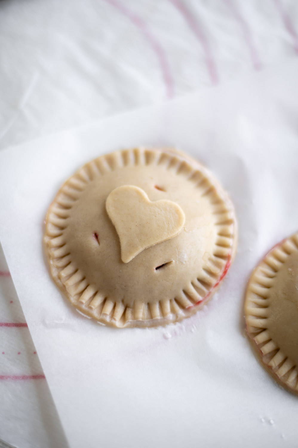 a Valentine's day cherry hand pie rests of a table ready to back decorated with a simple heart shape cut out