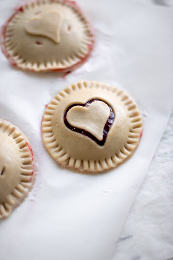 a Valentine's day cherry hand pie with a heart cut out rests on a baking sheet ready to place in the oven.