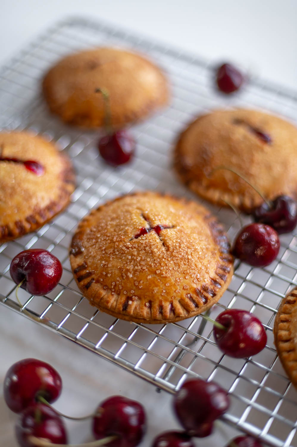 easy cherry hand pies rest on a cooling rack fresh out of the over next to a scattering of fresh cherries