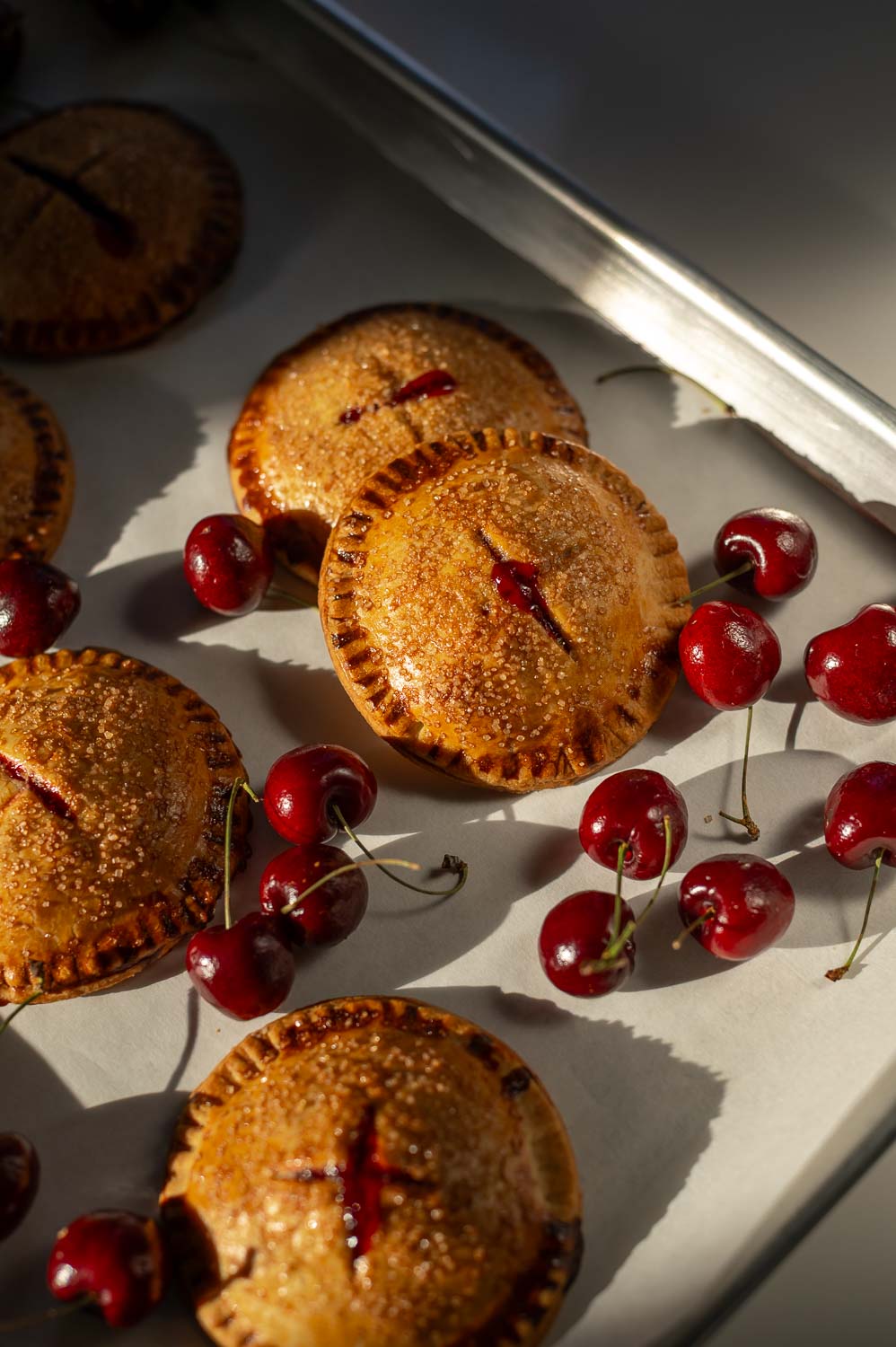 semi-homemade cherry hand pies fresh out of the oven on a baking sheet next to fresh cherries