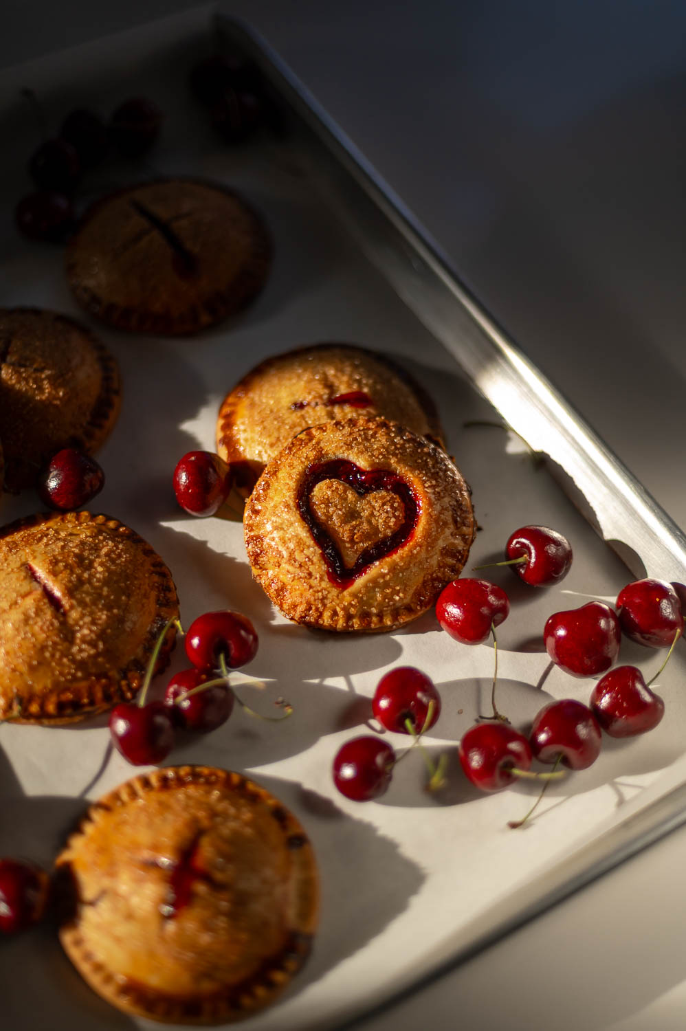 a Valentine's day cherry hand pie fresh out of the oven sits on a baking sheet next to fresh cherries
