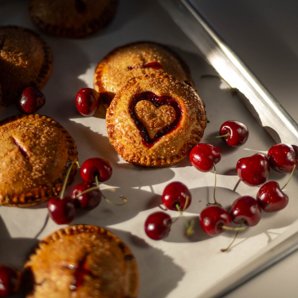 Easy Semi-Homemade Cherry Hand Pies With With Canned Filling rest on a baking sheet with fresh cherries