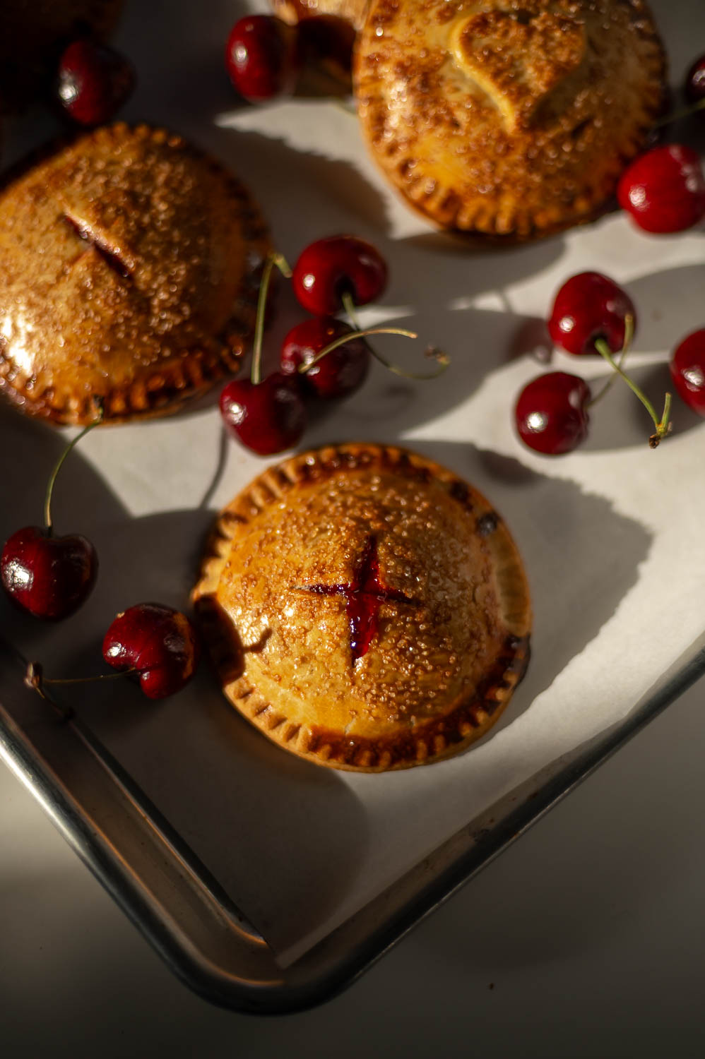semi-homemade cherry hand pies fresh out of the oven on a baking sheet next to fresh cherries