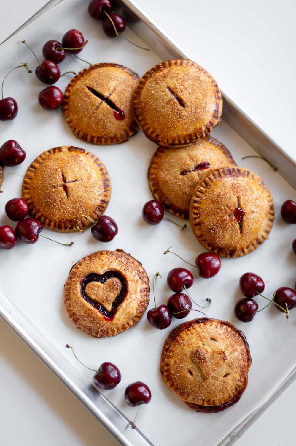 semi-homemade cherry hand pies for Valentine's day fresh out of the oven on a baking sheet next to fresh cherries