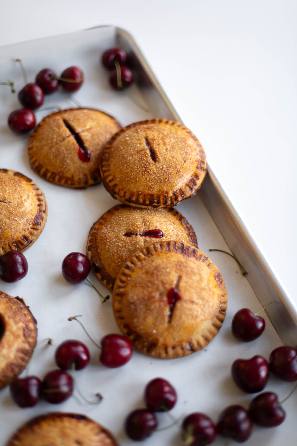 semi-homemade cherry hand pies fresh out of the oven on a baking sheet next to fresh cherries