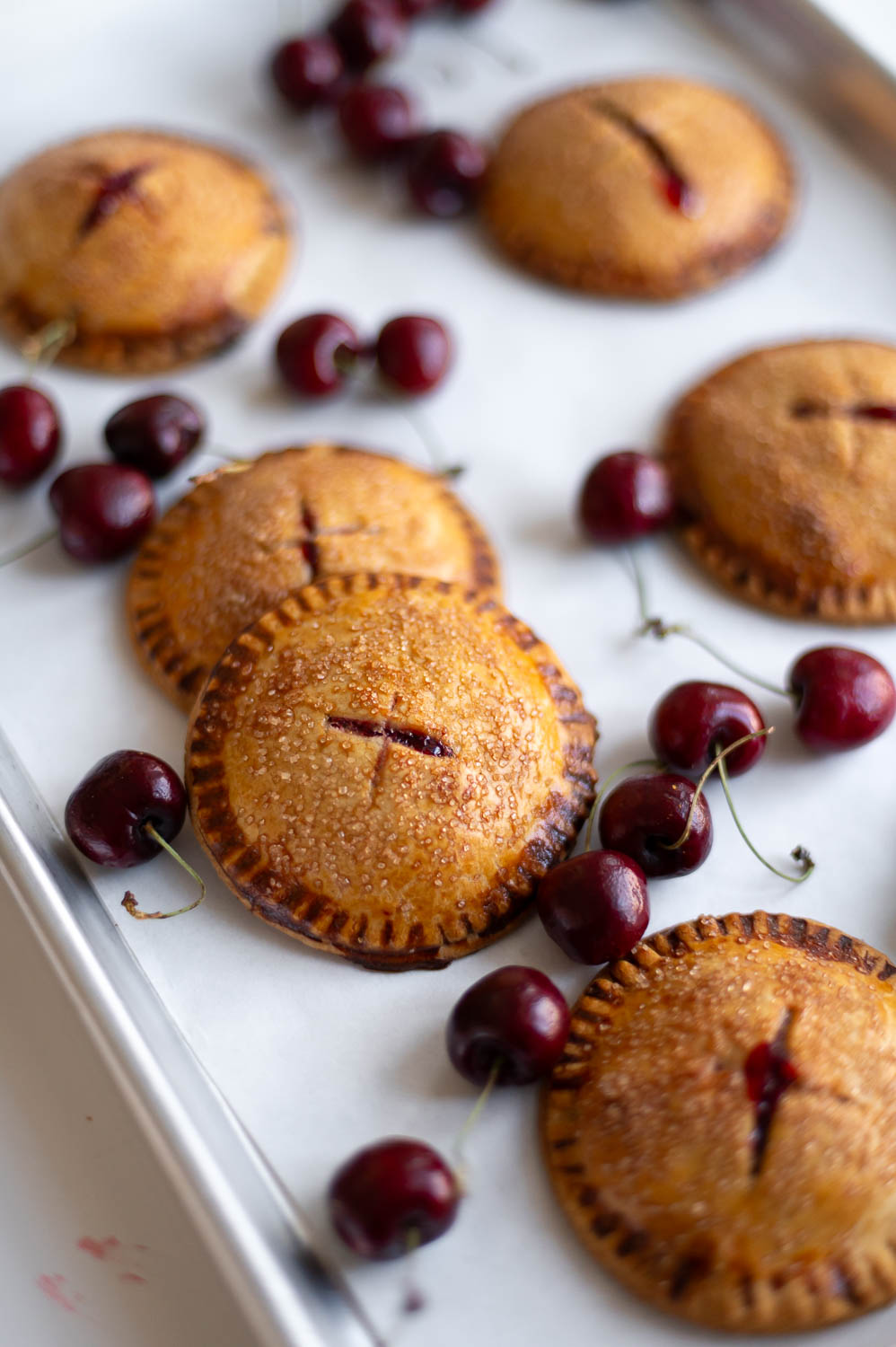 semi-homemade cherry hand pies fresh out of the oven on a baking sheet next to fresh cherries