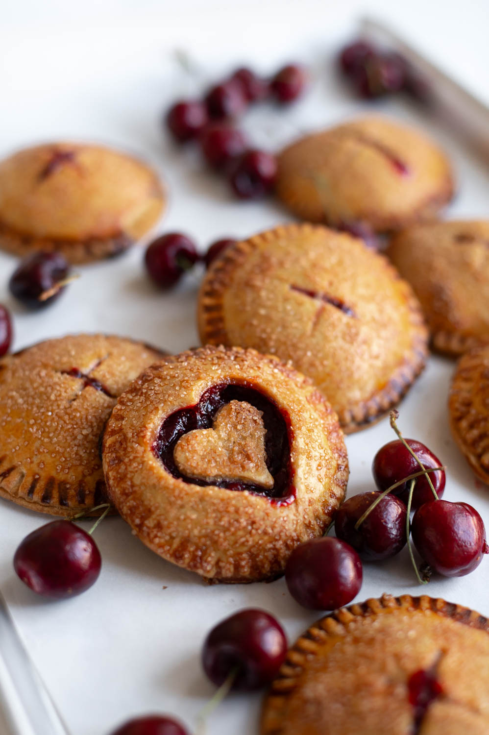 semi-homemade cherry hand pies fresh out of the oven for Valentine's day rest on a baking sheet next to fresh cherries