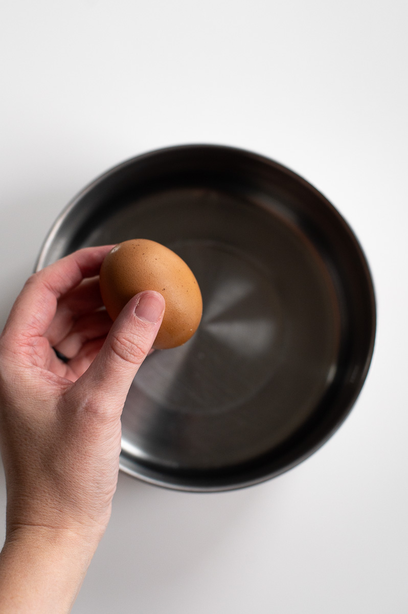 A woman places a brown egg in a vinegar soak to remove pigment from brown eggs in order to dye it pastel colors for easter