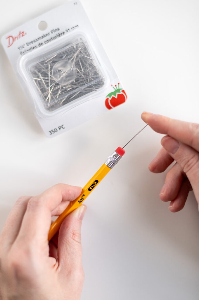 a woman places a dressmakers pin in the eraser end of pencil in order to create pin-drag drop pull wax designs on an easter egg
