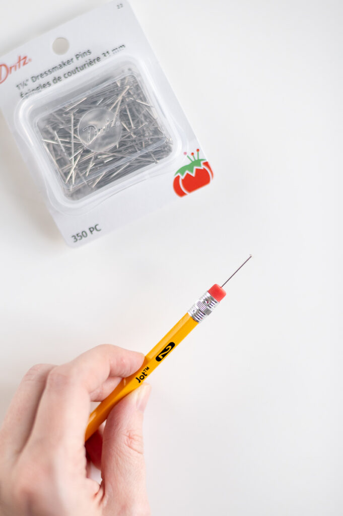 a woman holds a pencil with a dressmakers pin on the end in order to create pin-drag drop pull wax designs on an easter eggs
