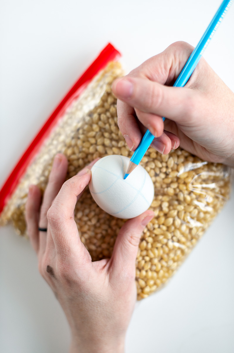 a woman apply guidelines on a white easter egg in order to decorate Easter eggs with traditional pysanky Easter egg wax designs