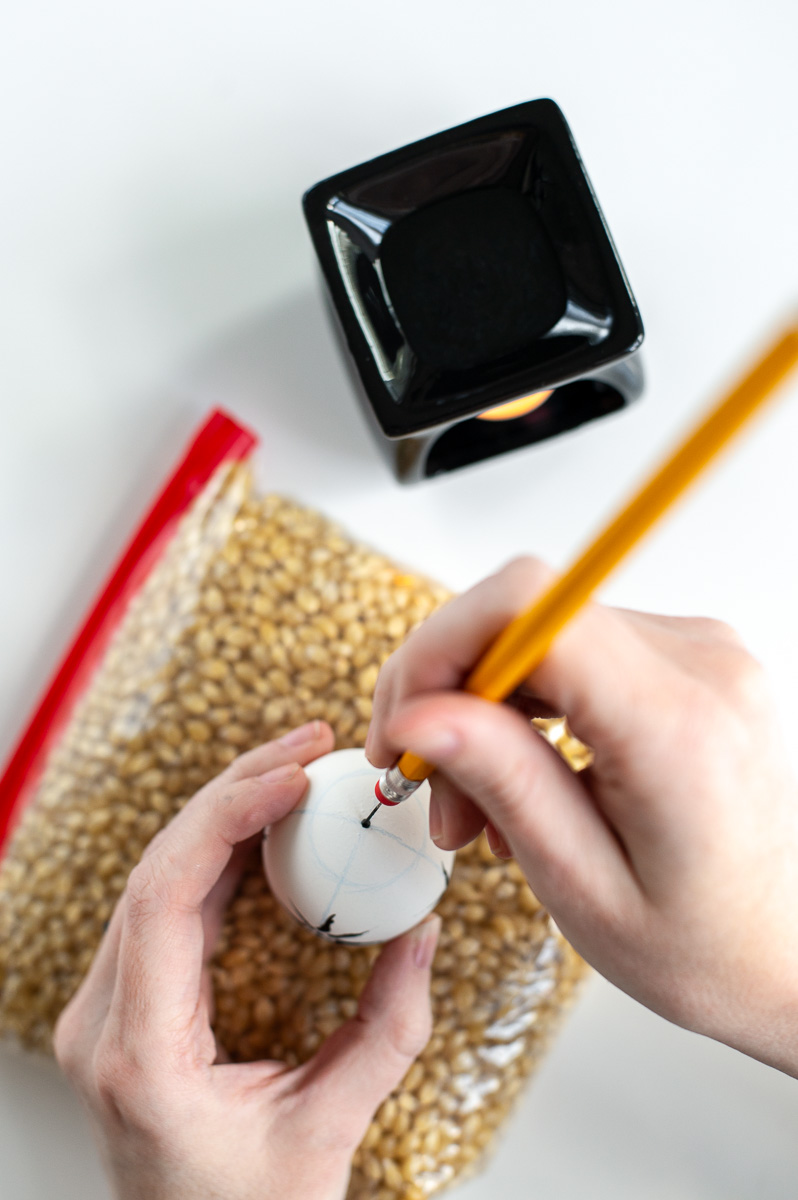 a woman makes a dot with hot wax using the pin-drag drop pull wax resist method for decorating easter eggs