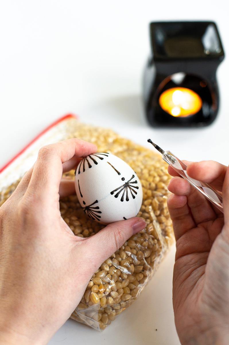 a woman show how to decorate easter eggs with wax using a traditional drop-pull wax application method.