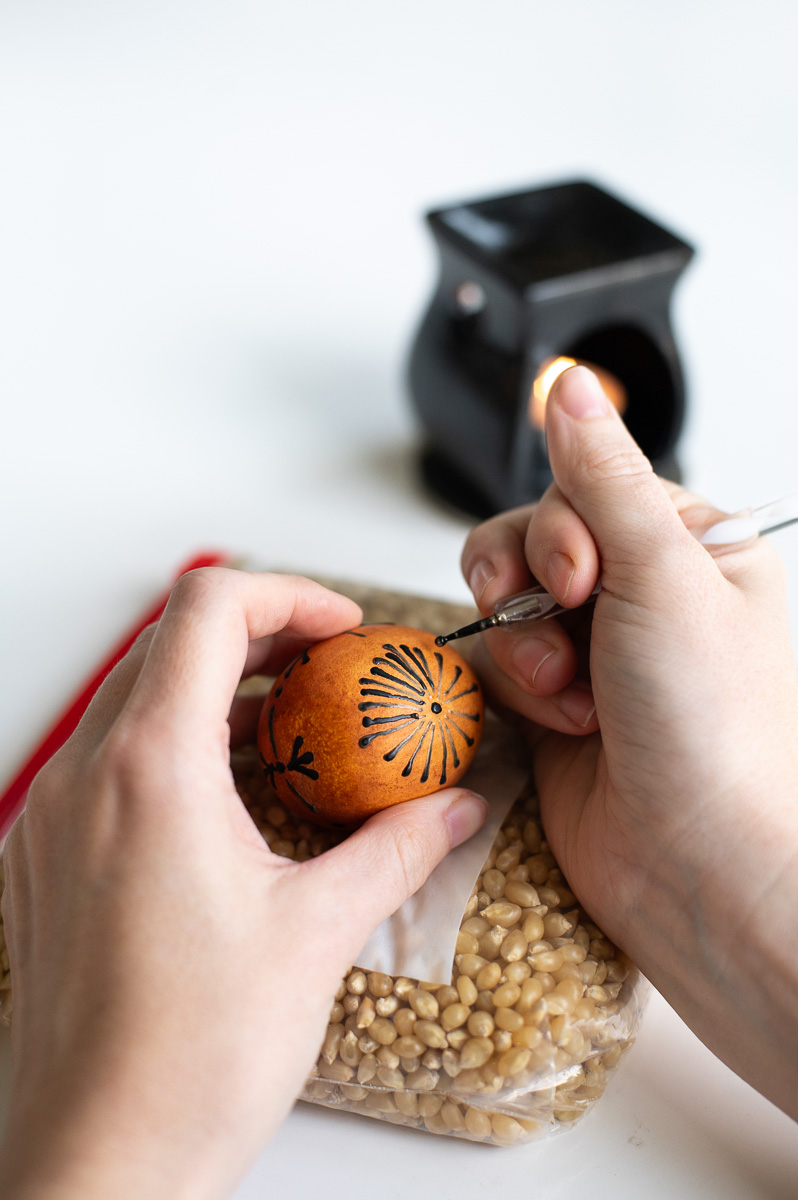 a woman applies a second round of wax to an easter egg after the first dye bath using traditional pysanky easter egg decorating methods without a kistka