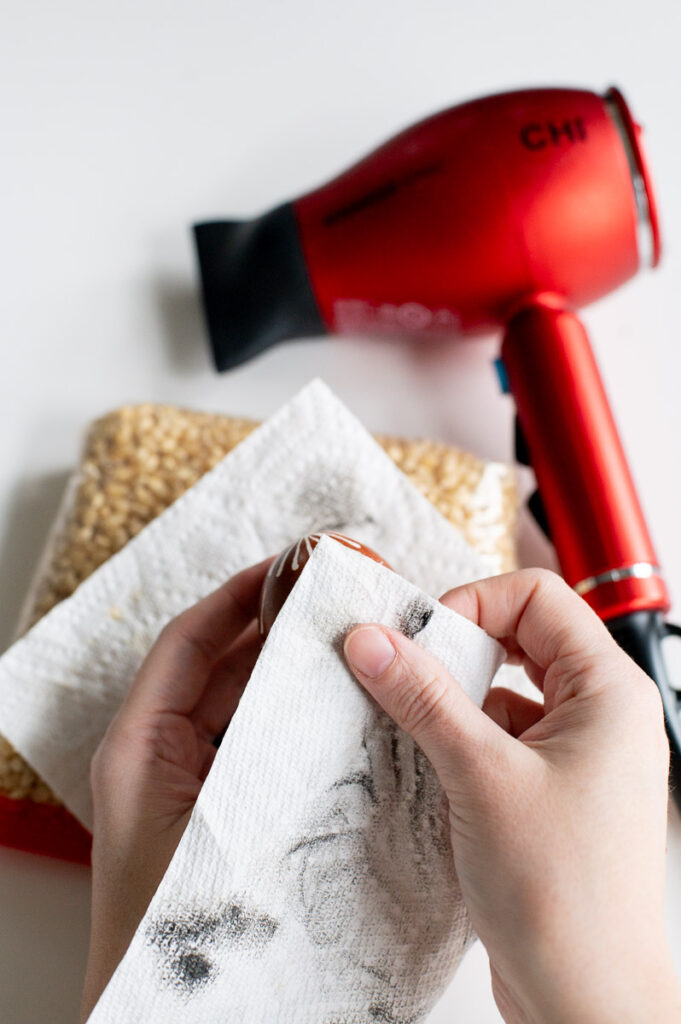 Removing wax from a DIY pysanky Easter egg with a paper towel to reveal the design