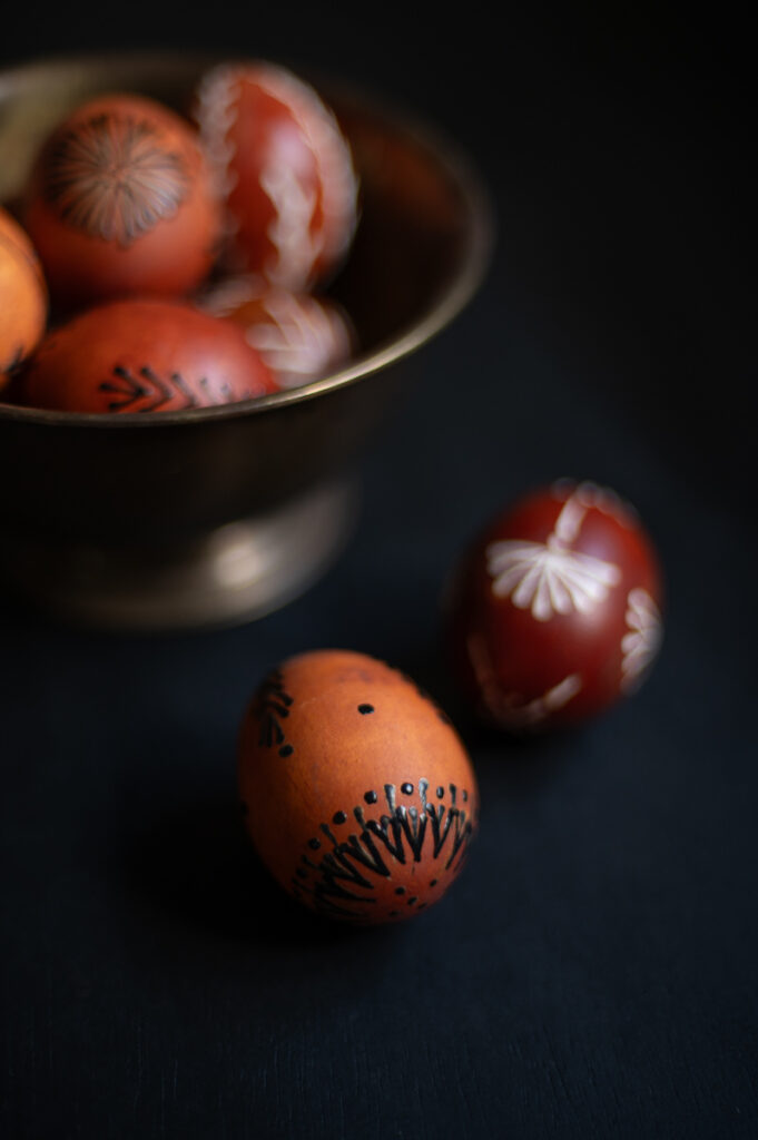 an example of a wax resist eggsdyed with onion skins using traditional drop-pull, pin-drag pysanky wax techniques laying on a table next to a bowl filled with easy pysanky easter eggs.