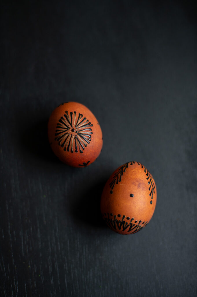 two easter eggs dyed with onion skins and decorated with wax lay on a black table as elegant traditional easter egg decor.
