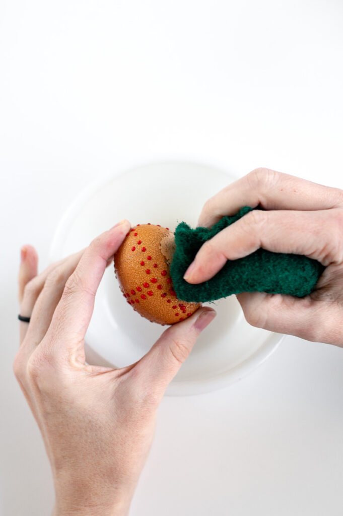 a woman uses hot water to remove the wax and scrub the vinegar off a brown egg.
