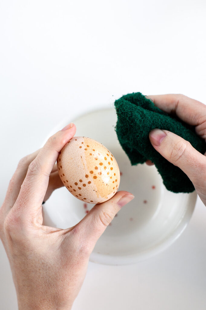 a woman scrubs a brown egg that has soaked in vinegar to reveal a lighter brown.